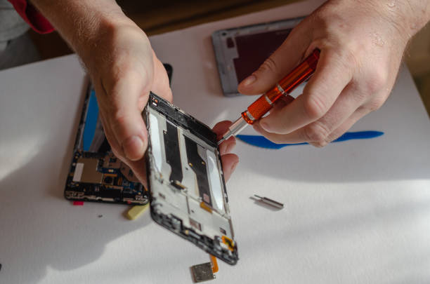 Repair of smartphones concept. A man unscrews the screws fixing the display from the board. Part of a series. Inside the room. Selective focus.